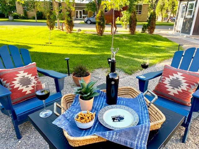 Blue Adirondack chairs and a table with red patterned pillows on the lawn